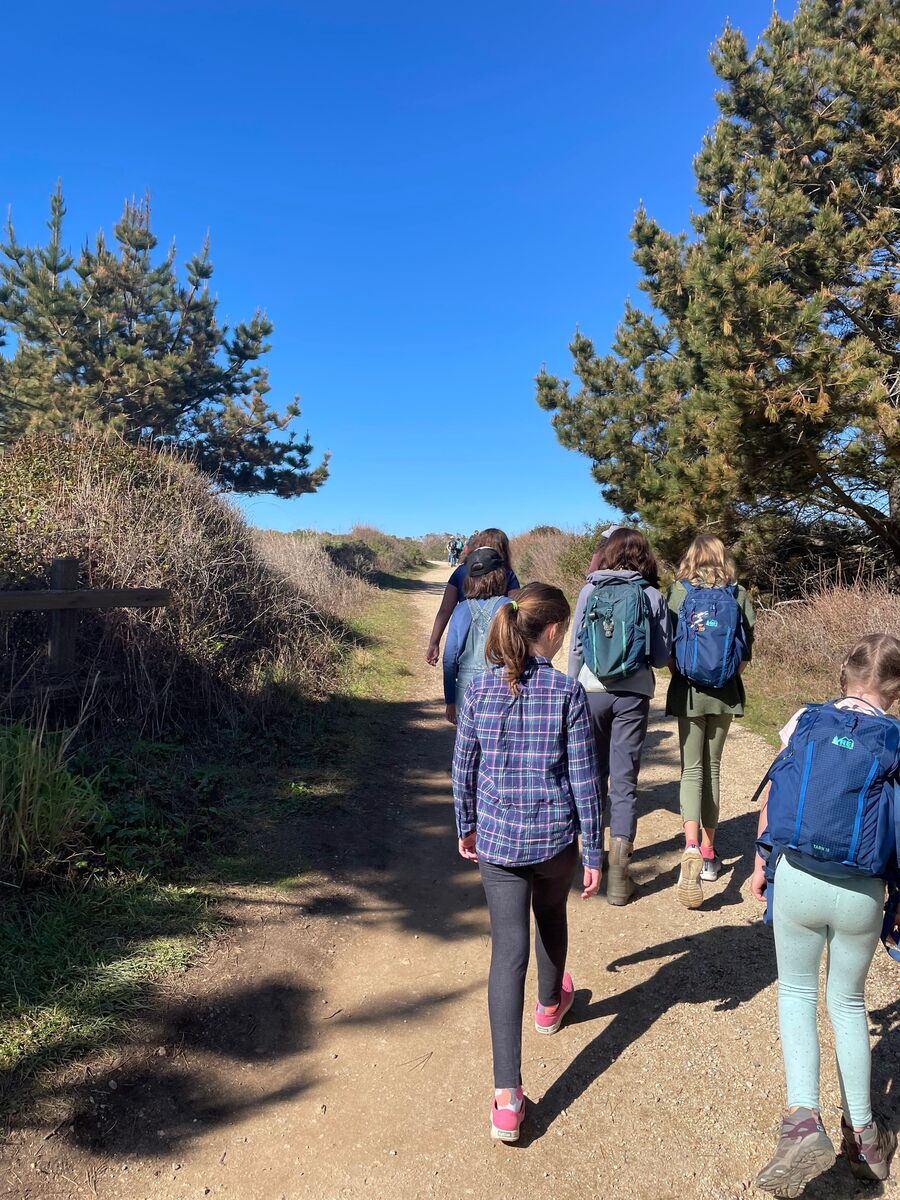 A group of children hiking along a dirt trail under a clear blue sky